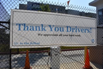 large white and blue banner hanging on entry fence reading "Thank you Drivers! Life, to the fullest"