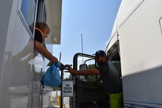 A TSG associate welcomes a truck driver pulling through the entrance with a swag bag, drinks, and snacks